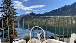 En balkong med ett bord dukat för te, med utsikt över en stilla sjö och berg.