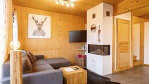 Ein gemütliches Wohnzimmer mit grauem Sofa, einem Holztisch, einem Flachbildfernseher und einem Kamin.