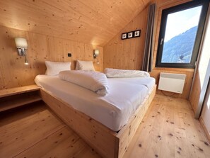 Ein Schlafzimmer einer Holzhütte mit einem Bett, Nachttischlampen und einem Fenster mit Blick auf die Berge.