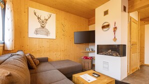 Ein gemütliches Wohnzimmer mit einer Eckcouch, einem Flachbildfernseher, einem Kamin und einer Holzwand mit Dekorationselementen.
