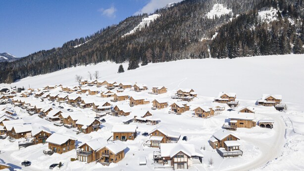 A snow-covered village with wooden houses, a mountain in the background, and a clear sky.
