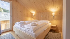 A wooden bedroom with a bed, two wall-mounted lights, and a view of a wooden deck outside.