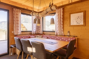 A wooden dining area with a large table and chairs, a hanging light fixture, and a window with curtains. - Superior Chalet # 55 with IR-Sauna (Hohentauern)