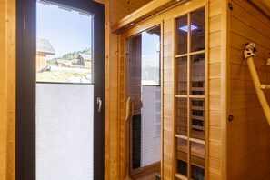 A wooden sauna room with a glass door, a bench, and a towel rack.