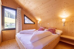 A wooden cabin bedroom with a large bed, two bedside tables, a window with curtains, and a view of a forested area. - Superior Chalet # 55 with IR-Sauna (Hohentauern)