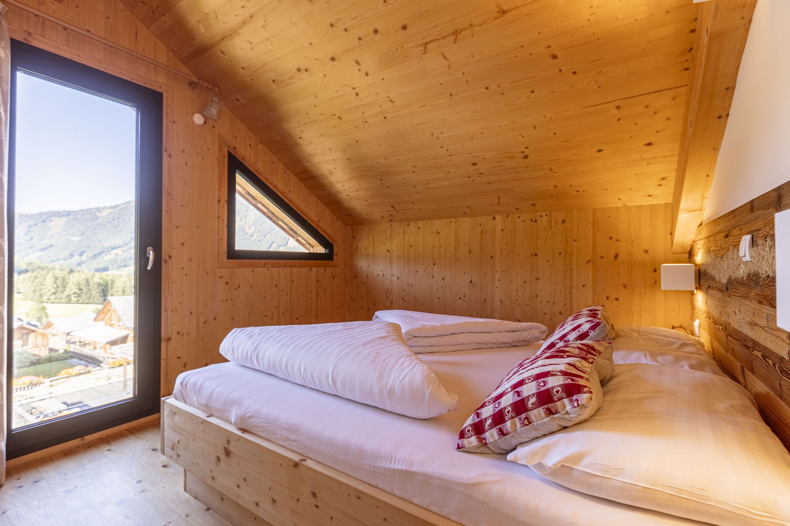 Une chambre dans une cabane en bois, avec un lit, des oreillers et une fenêtre donnant sur une région montagneuse.