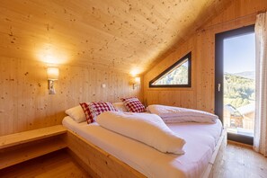 A wooden cabin bedroom with two beds, a window, and a view of the outside.