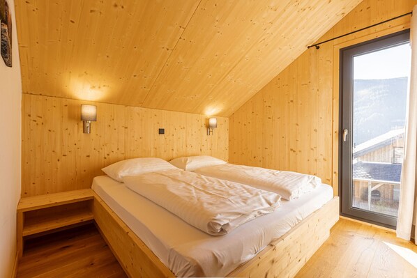 A wooden room with a bed, two wall-mounted lights, and a window.