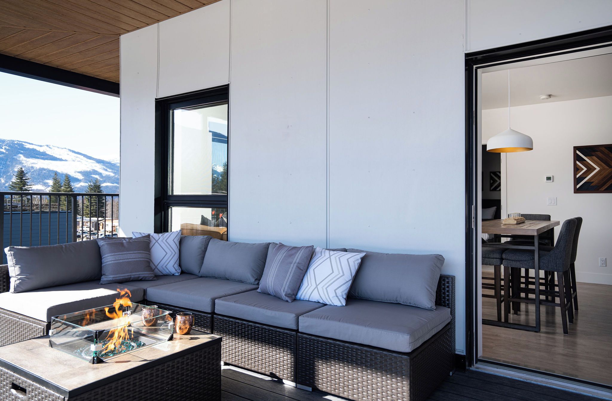 A modern outdoor seating area with a sofa and a glass-top table, a view of mountains, and a dining area with a table and chairs.