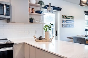 Een moderne keuken met witte kasten, een inbouwmagnetron, een fornuis en een eethoek met een tafel en stoelen.