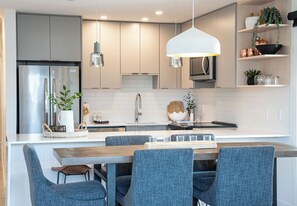 Een moderne keuken met een centraal eiland, roestvrijstalen apparatuur en een hangende pendelarmatuur.