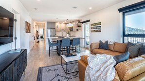 A modern living room with a sofa, a coffee table, and a view of a kitchen and dining area. - The Big Deck by Revelstoke Vacations (Revelstoke)