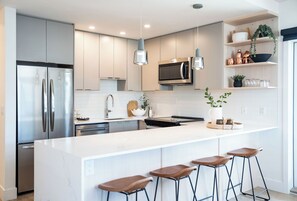 Een moderne keuken met roestvrijstalen apparatuur, witte keukenkastjes en een centraal kookeiland met barkrukken.