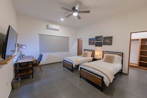 Ein Schlafzimmer mit zwei Betten, einem Schreibtisch, einem Stuhl, einem Deckenventilator und einem Kleiderschrank.