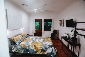 A bedroom with a bed, a desk, a chair, a TV, and a window with curtains.