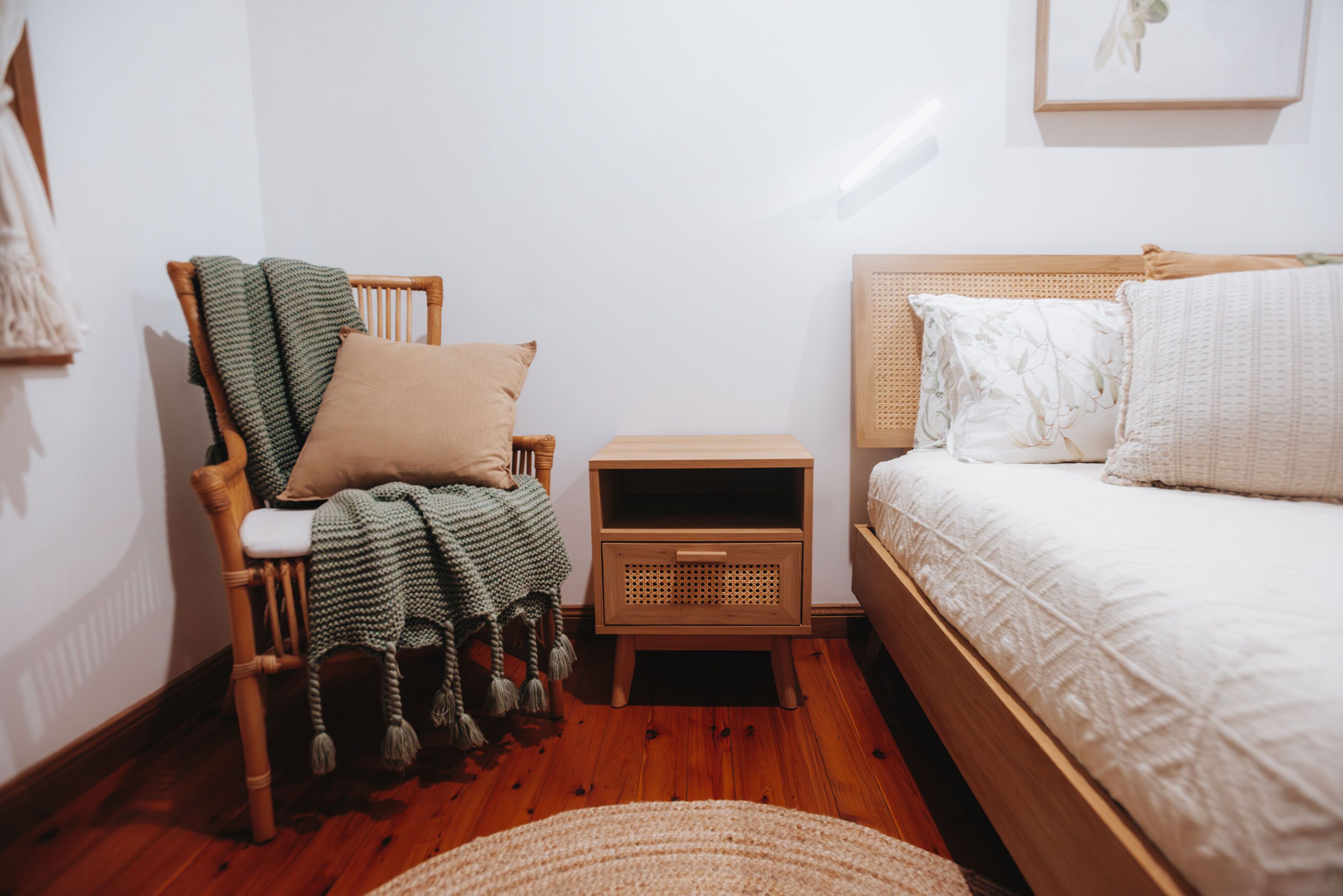 A cozy bedroom with a wooden chair, a bedside table, and a bed with white bedding.