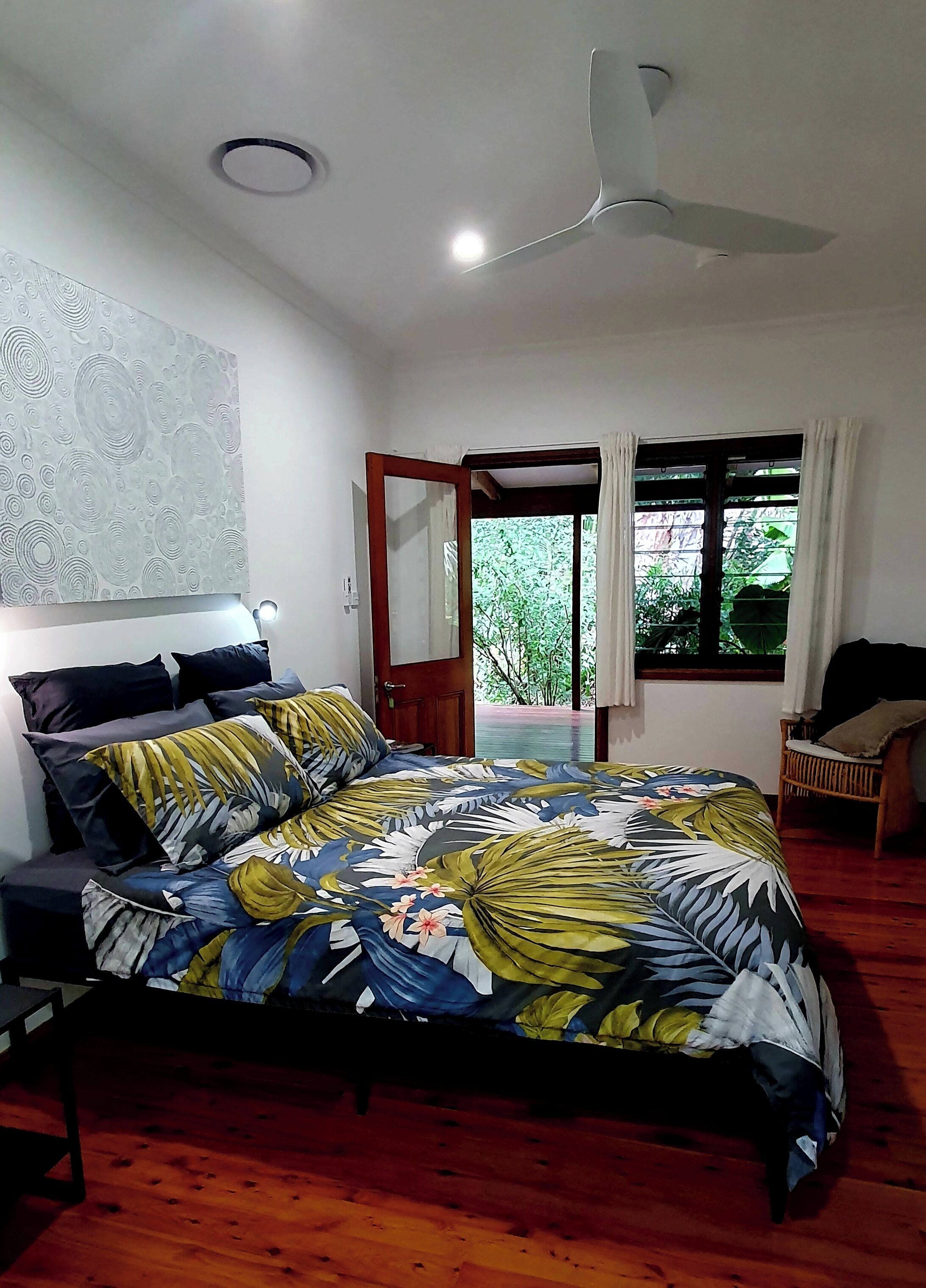 A bedroom with a bed, a ceiling fan, a window with curtains, and a view of greenery outside.