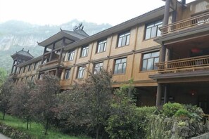 Un immeuble à plusieurs étages, doté d’éléments architecturaux traditionnels, de balcons et surplombant un paysage montagneux.