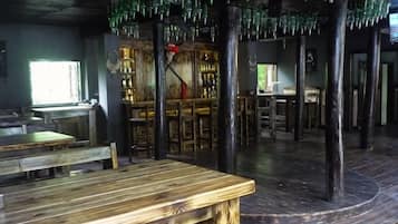 Un intérieur rustique avec des tables et des chaises en bois, un coin bar et un plafond original orné de bouteilles en verre suspendues.