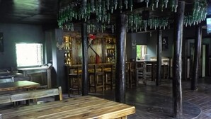Ein rustikaler Innenraum mit Holztischen und -stühlen, einer Bar und einer besonderen Decke mit hängenden grünen Glasflaschen.
