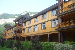 Un hotel de varios pisos con balcones y un paisaje montañoso al fondo.