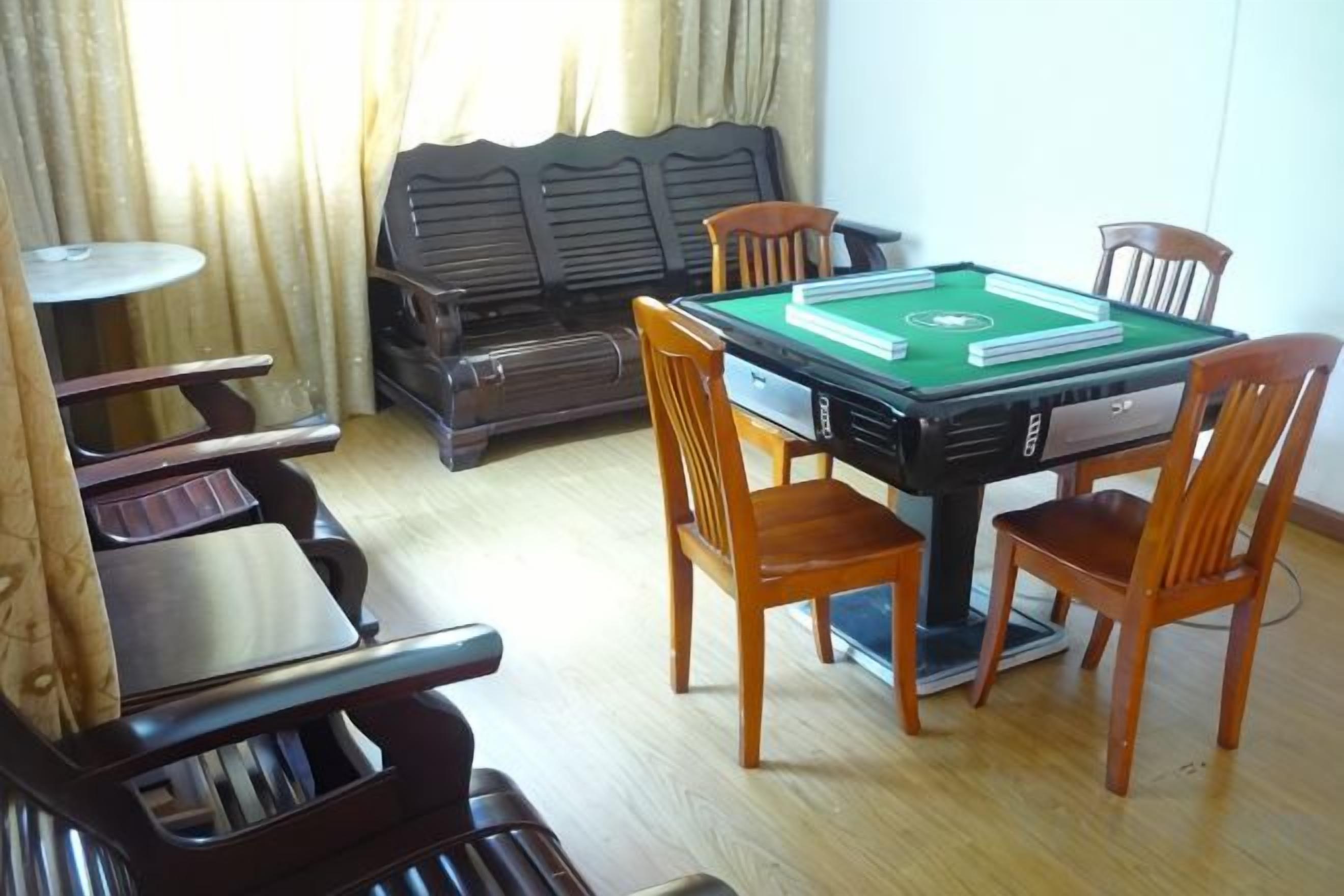 A pool table with four chairs, a sofa, and a small round table in a room with wooden flooring.