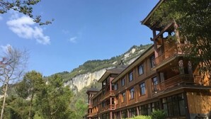 Ein mehrstöckiges Holzgebäude mit Balkonen, umgeben von Bäumen und mit Blick auf eine Bergkulisse.