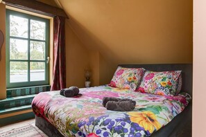 Une chambre à coucher avec un grand lit, une literie à motifs floraux, une fenêtre avec des rideaux et une vue sur l’extérieur.