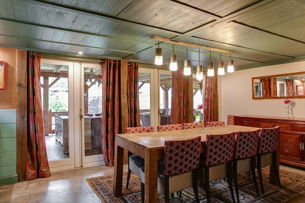 A dining area with a wooden table and chairs, a hanging light fixture, and a view through a glass door.