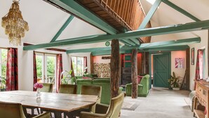 A dining area with a wooden table and chairs, a chandelier, and a green sofa. - BoHo Experience - Jacuzzi, Sauna, BBQ, Garden, close to Amsterdam - Sleeps 10 (Kockengen)