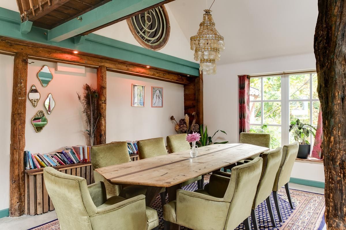 Een eetruimte met een houten tafel, groene bekleden stoelen en een kroonluchter.