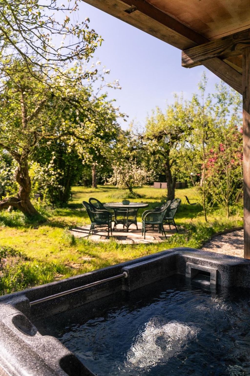 Een hottubgedeelte met een tafel en stoelen, omgeven door bomen en gras.
