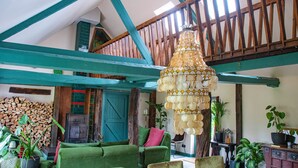 A spacious loft with a high ceiling, exposed wooden beams, a large chandelier, and a cozy seating area with a green sofa and armchairs. - BoHo Experience - Jacuzzi, Sauna, BBQ, Garden, close to Amsterdam - Sleeps 10 (Kockengen)