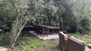 An outdoor dining area with a wooden table and chairs, surrounded by dense foliage.