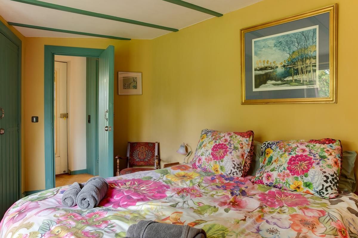 Une chambre à coucher avec une couvre-lit à motifs floraux, un tableau accroché au mur et une porte donnant sur une autre pièce.