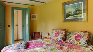 Une chambre à coucher avec une couvre-lit à motifs floraux, un tableau accroché au mur et une porte donnant sur une autre pièce.