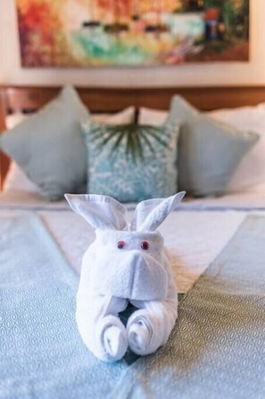 Uma cama bem arrumada com um coelho de toalha no centro, um cobre-leito azul estampado e almofadas azul claro.