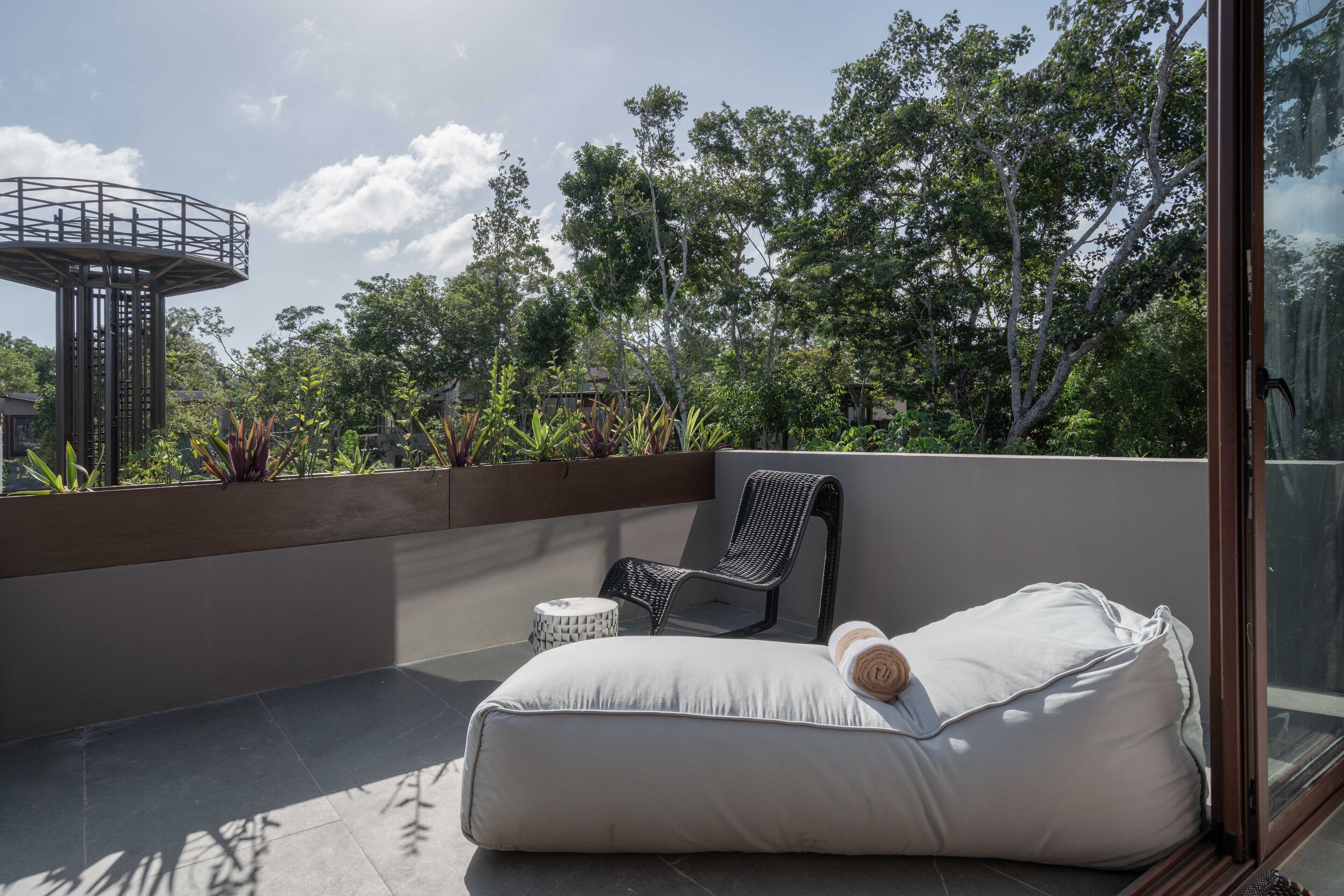 A balcony with a white cushioned seating area, a wicker chair, and a small round table.