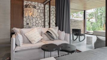 A modern bedroom with a stone wall, a grey sofa with cushions, a black chair, and a small round table.