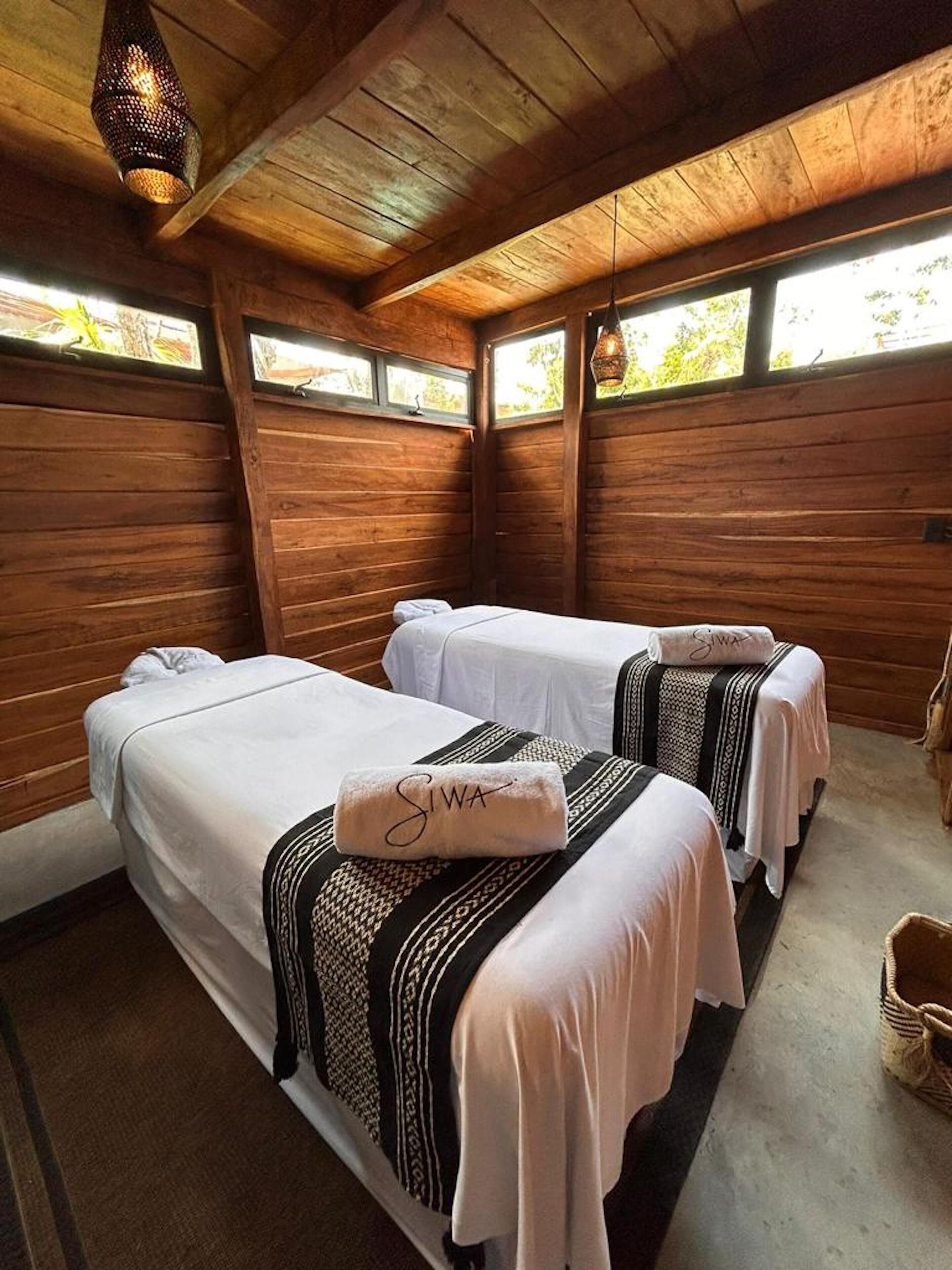 Una habitación con dos camas, paredes de madera y una lámpara colgante.