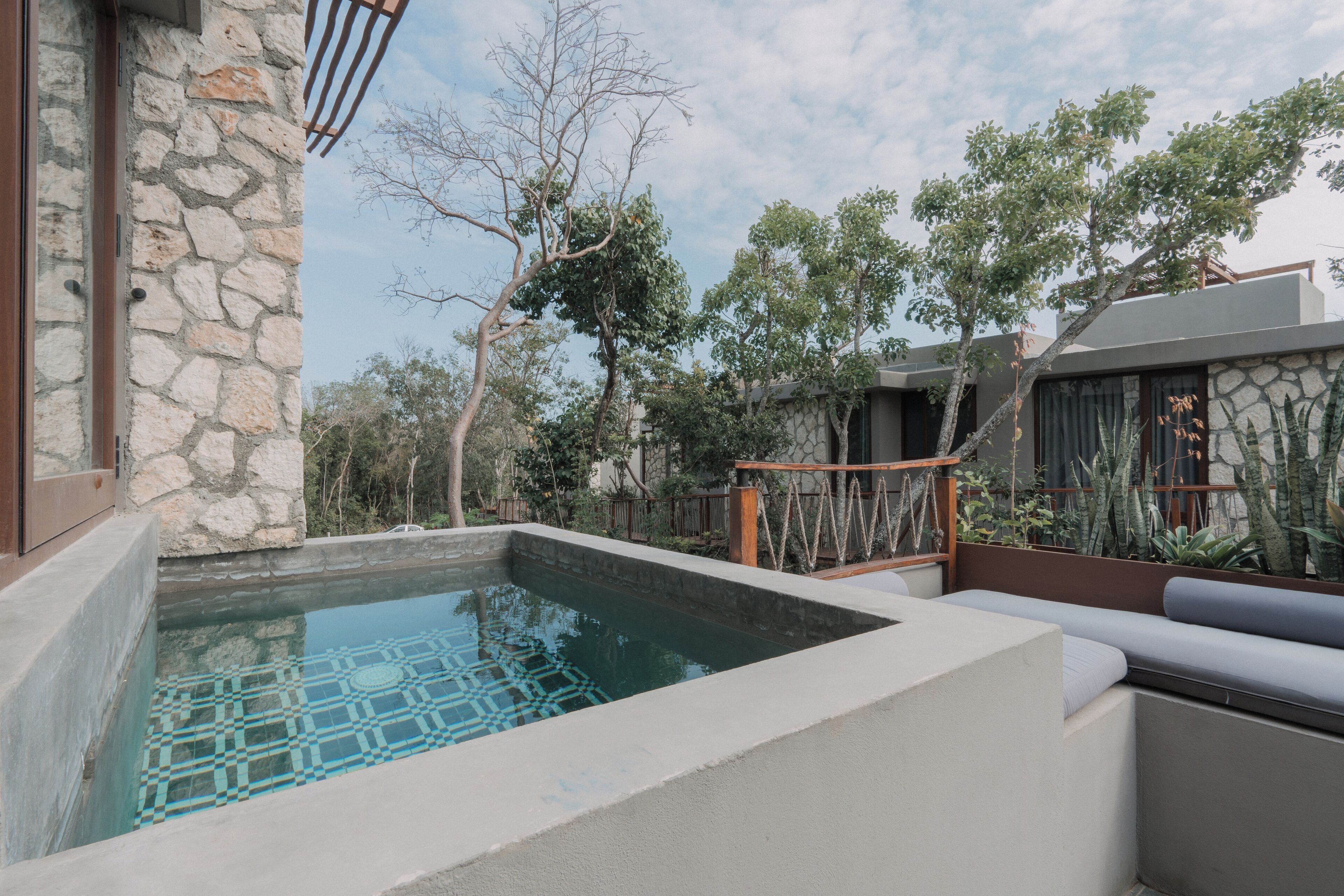 A modern outdoor pool area with stone walls, a seating area, and surrounding vegetation.