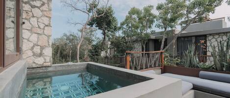 A modern outdoor pool area with stone walls, a seating area, and surrounding vegetation.