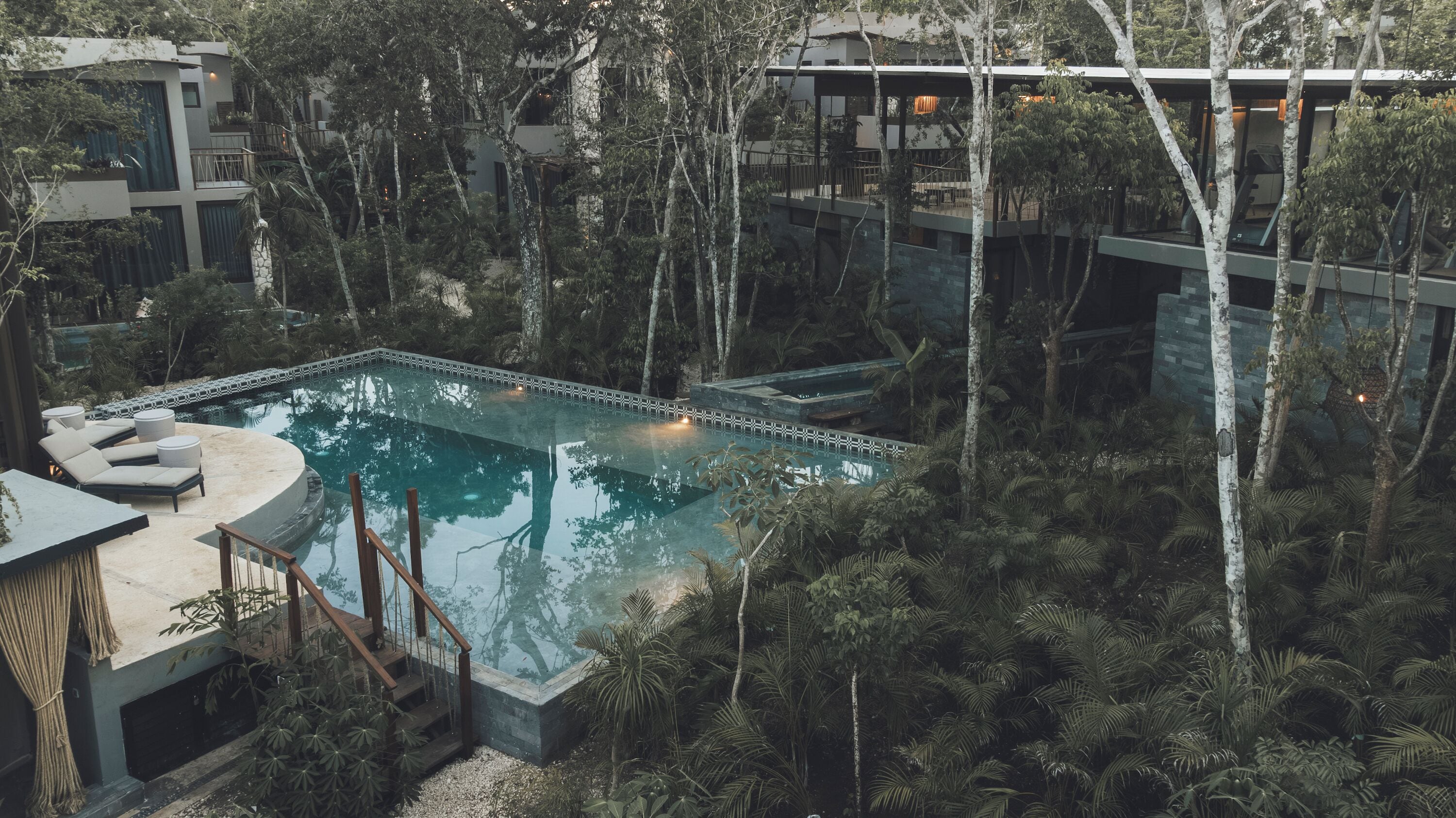 A modern outdoor pool surrounded by lush greenery and trees, with a contemporary building in the background.