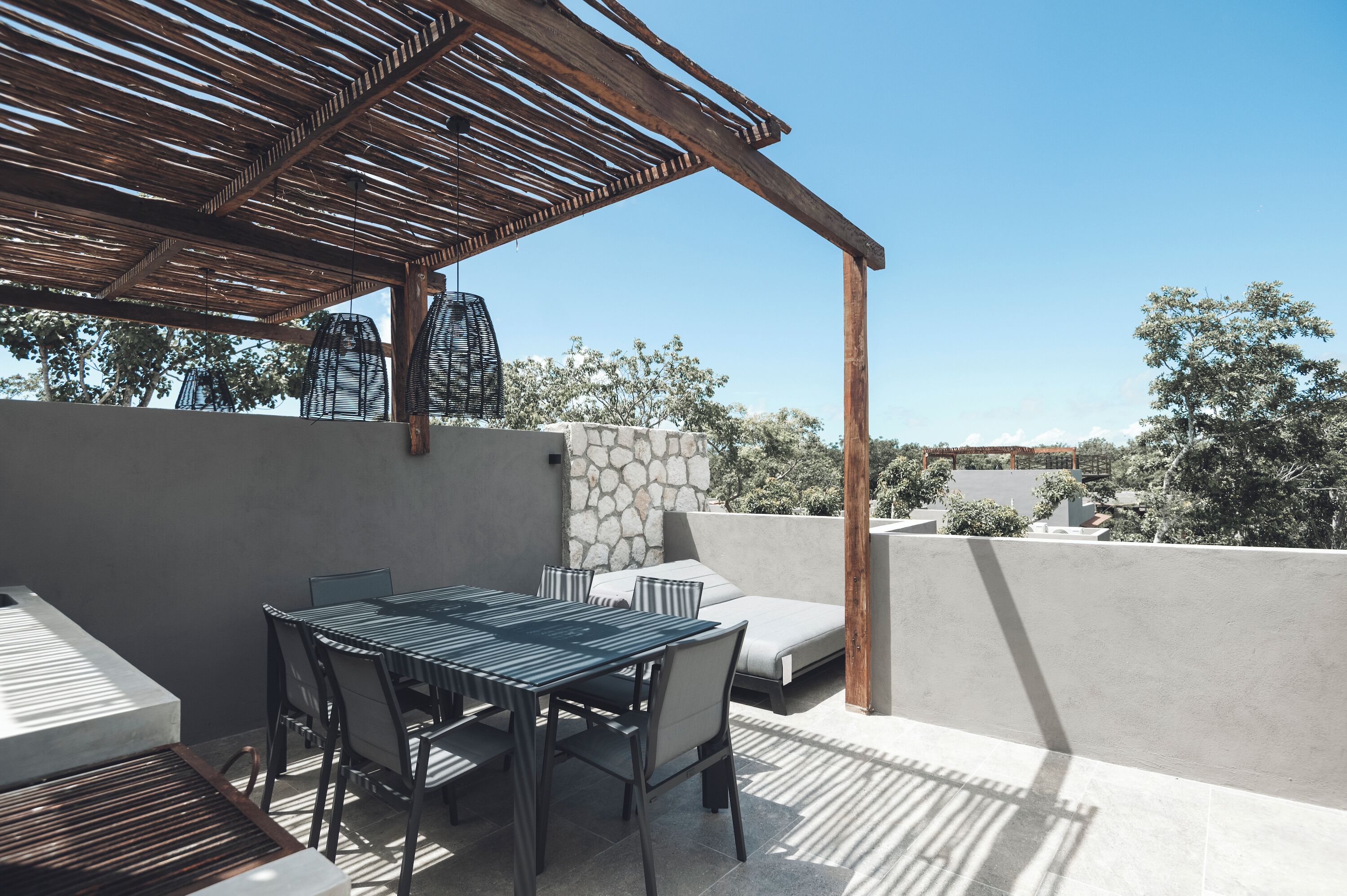 An outdoor patio with a table and chairs, a stone wall, and a pergola.