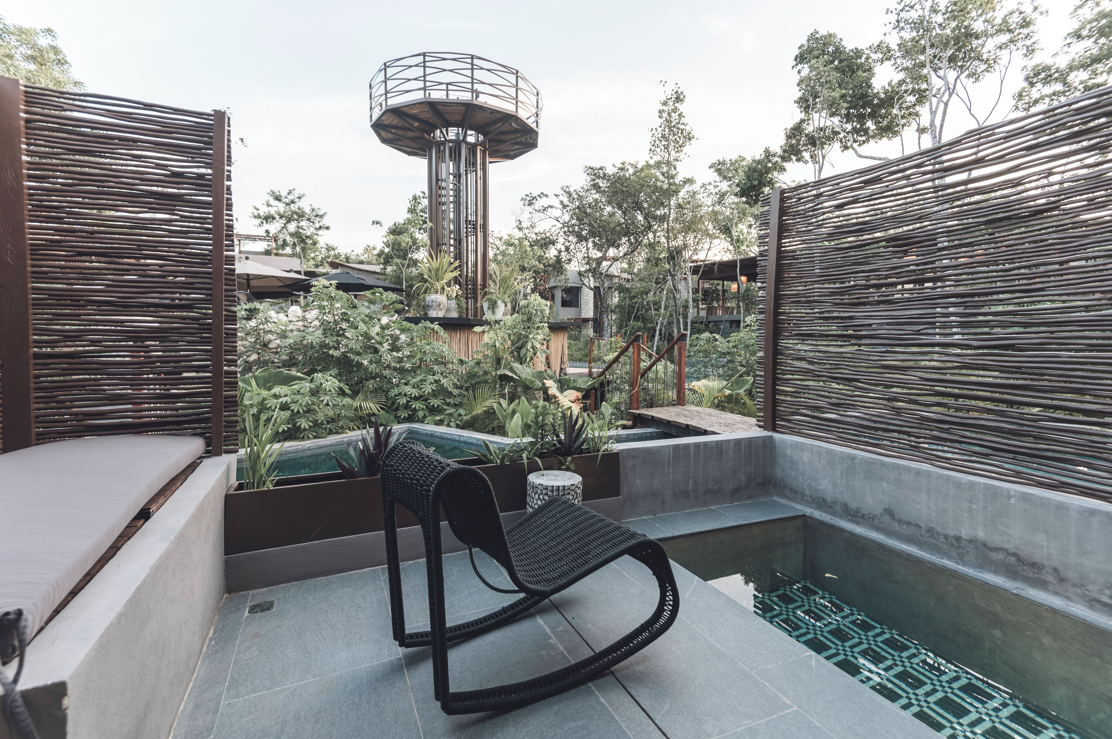 A rooftop terrace with a black rocking chair, a small pool, and surrounding greenery.