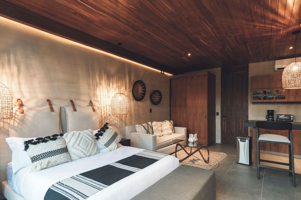 A modern bedroom with a bed, a sofa, a coffee table, and a small kitchen area with a bar stool.