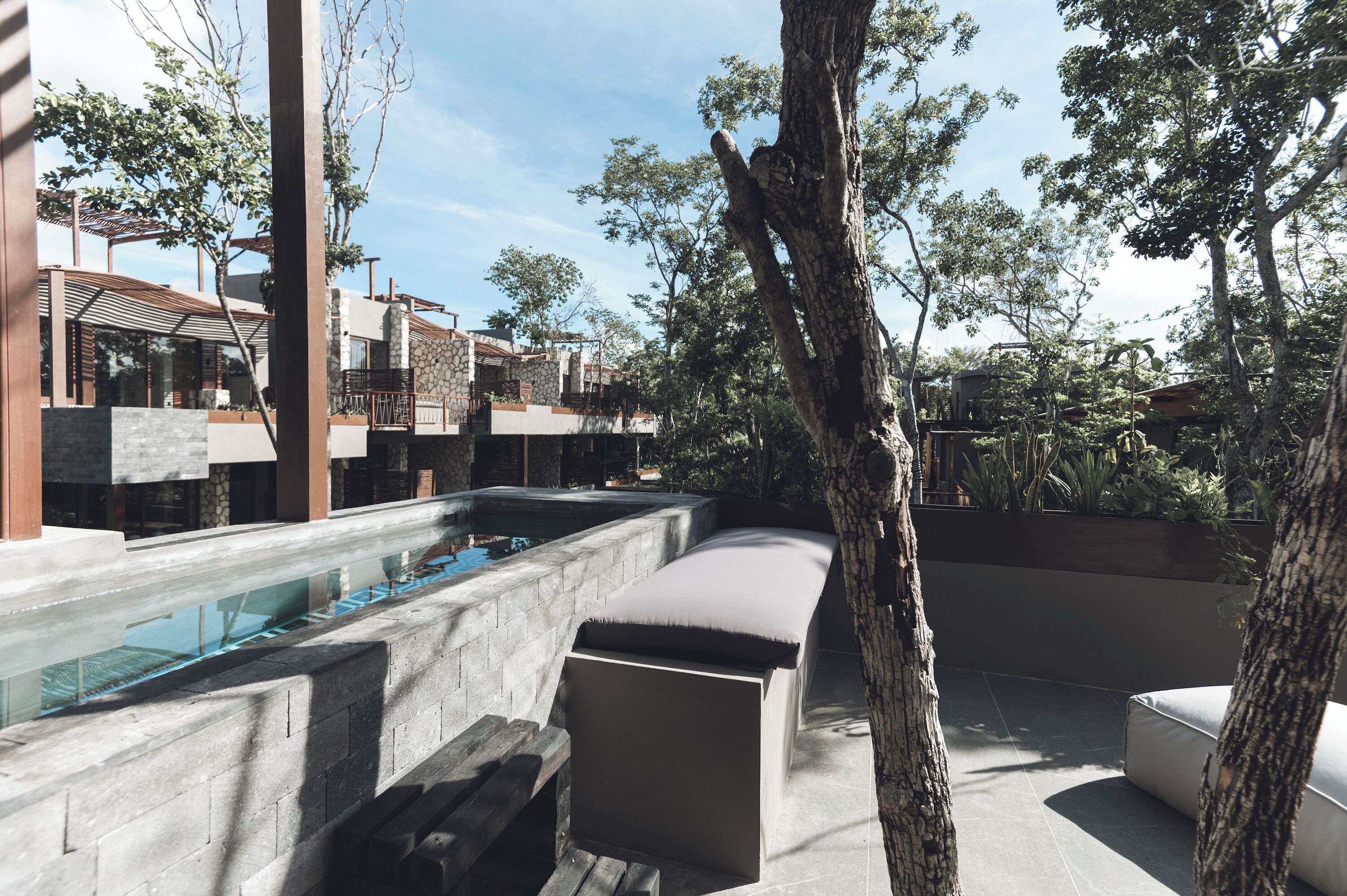 A modern outdoor pool area with a built-in bench, surrounded by stone walls and greenery.