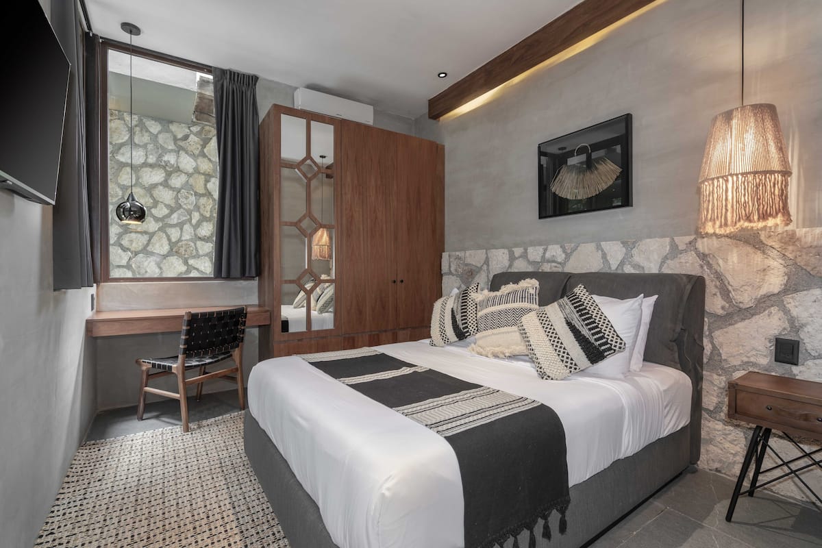 A bedroom with a bed, a desk, a chair, a wardrobe, and a hanging lamp.