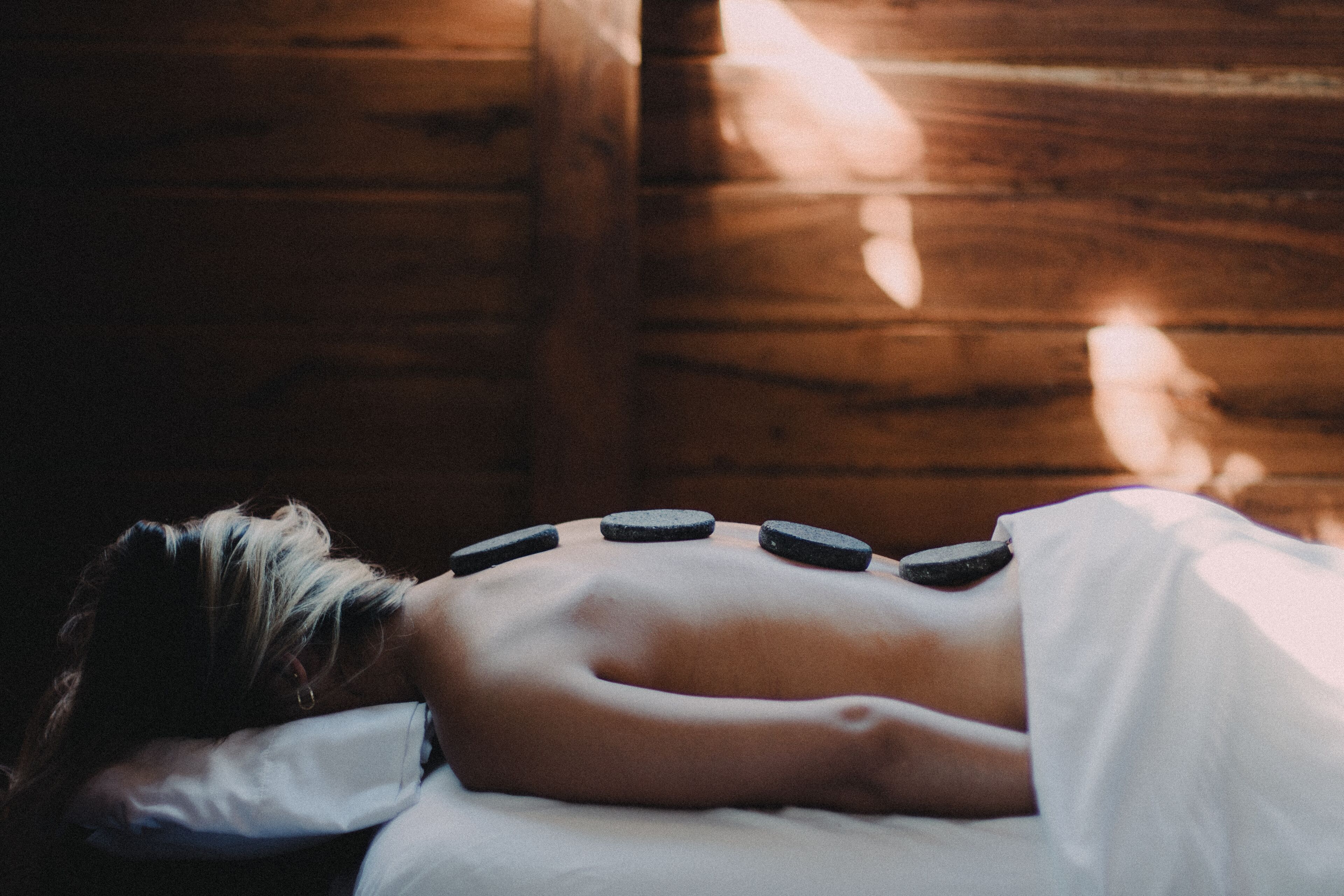 Une personne allongée sur un lit dont la tête de lit est en bois, recouverte d’un drap blanc.