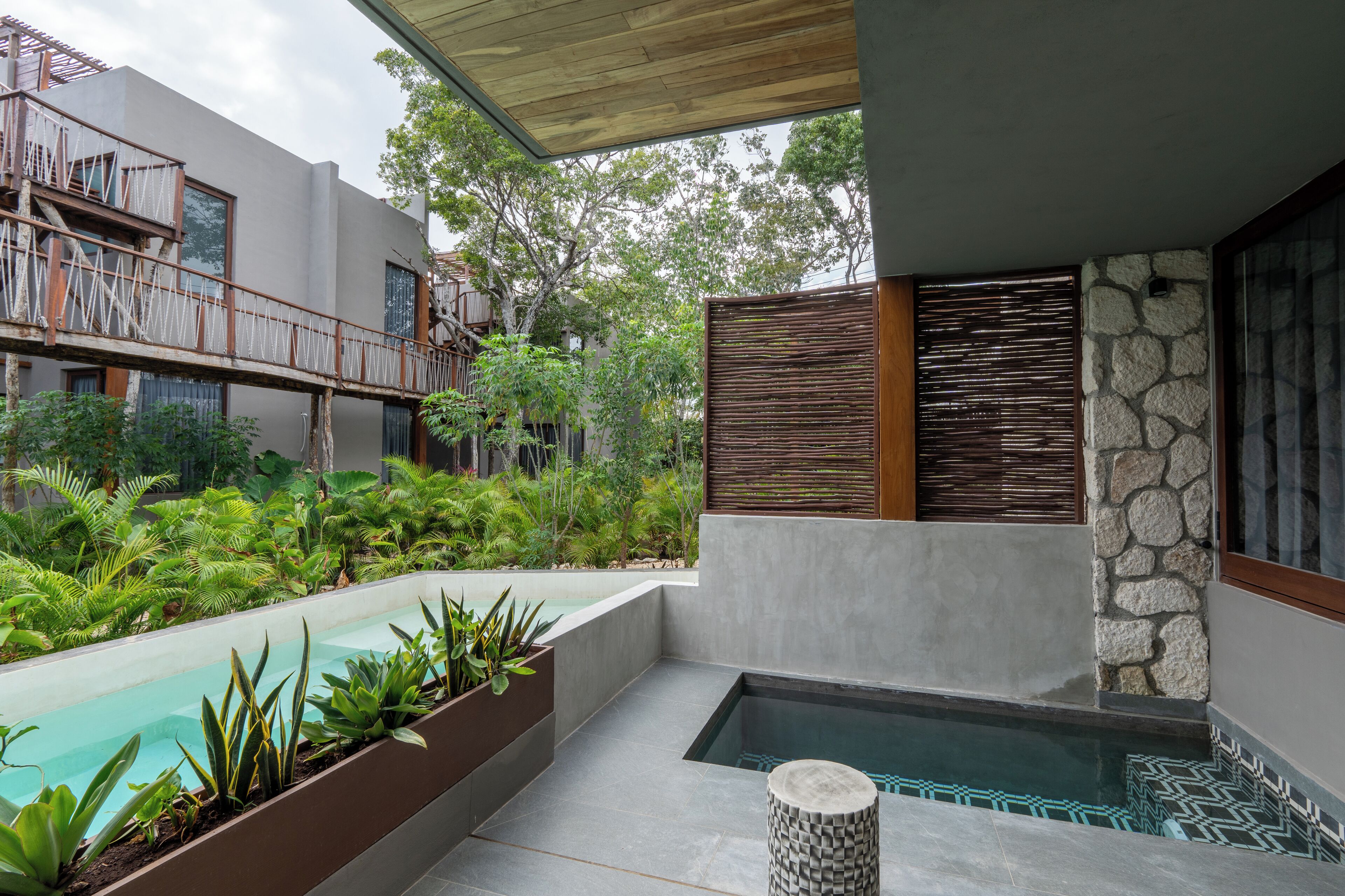 A modern outdoor pool area with a built-in jacuzzi, surrounded by lush greenery and a wooden deck.